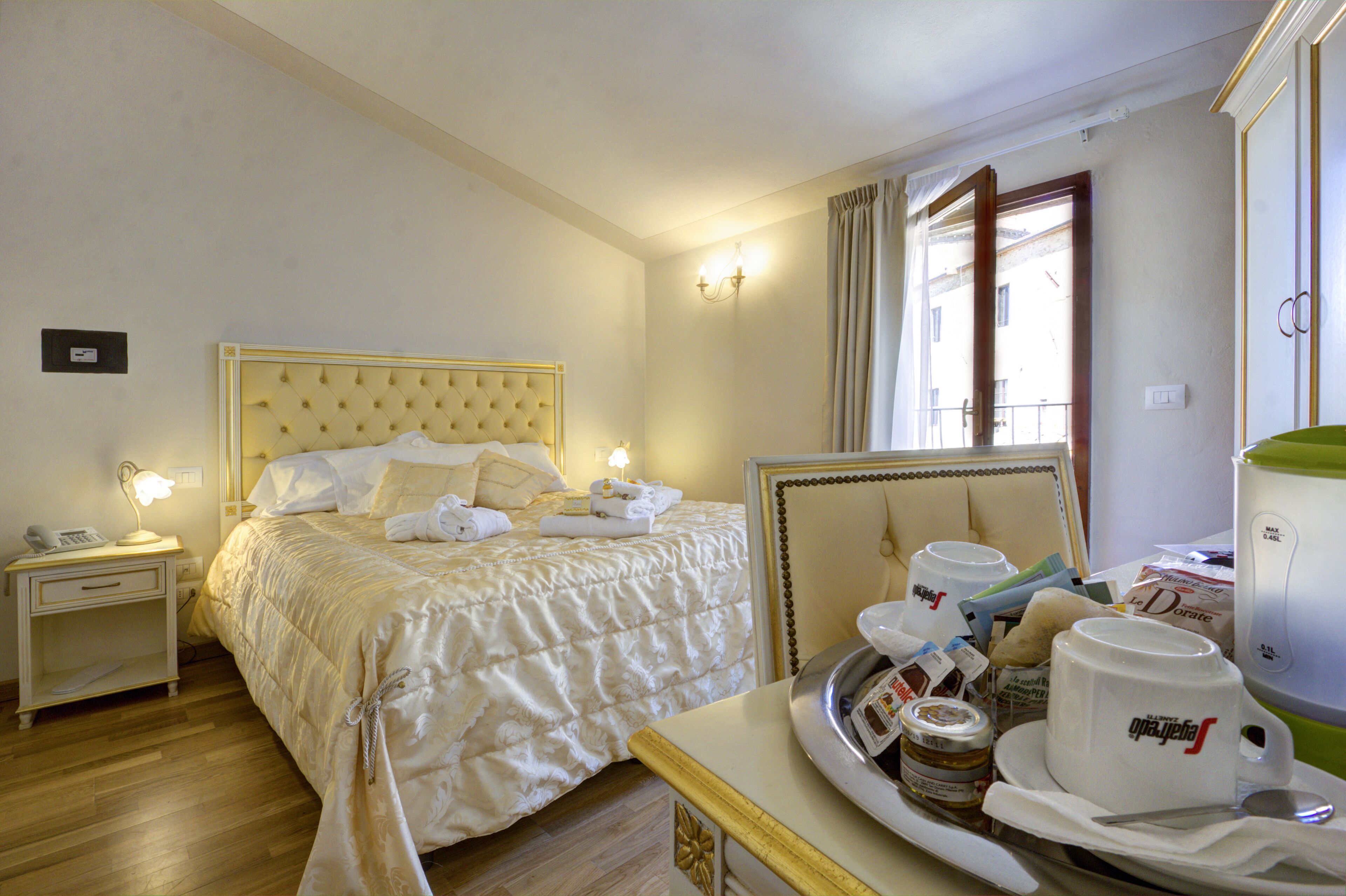 Habitación de hotel con una cama grande, mesitas de noche con lámparas, una bandeja con alimentos para el desayuno y vistas al exterior a través de una ventana.
