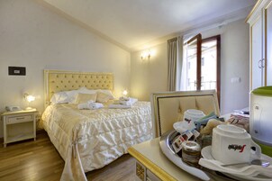 Habitación de hotel con una cama grande, mesitas de noche con lámparas, una bandeja con alimentos para el desayuno y vistas al exterior a través de una ventana.