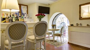 Un comedor con dos sillas ornamentales, una mesa con un jarrón de flores rojas y un televisor montado en la pared.