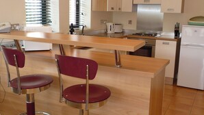Una cocina moderna con encimera de madera, dos sillas rojas, electrodomésticos de acero inoxidable y una ventana con persianas.