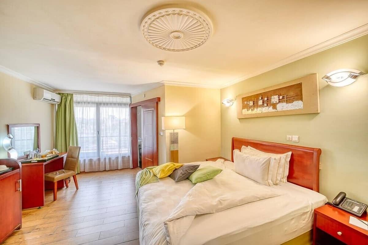 A hotel room with a bed, desk, chair, and a painting on the wall.