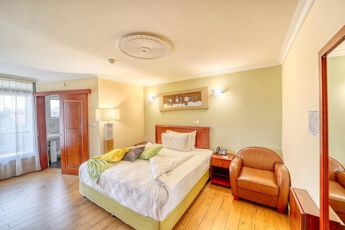 A hotel room with a bed, a chair, a nightstand, a lamp, and a painting on the wall.