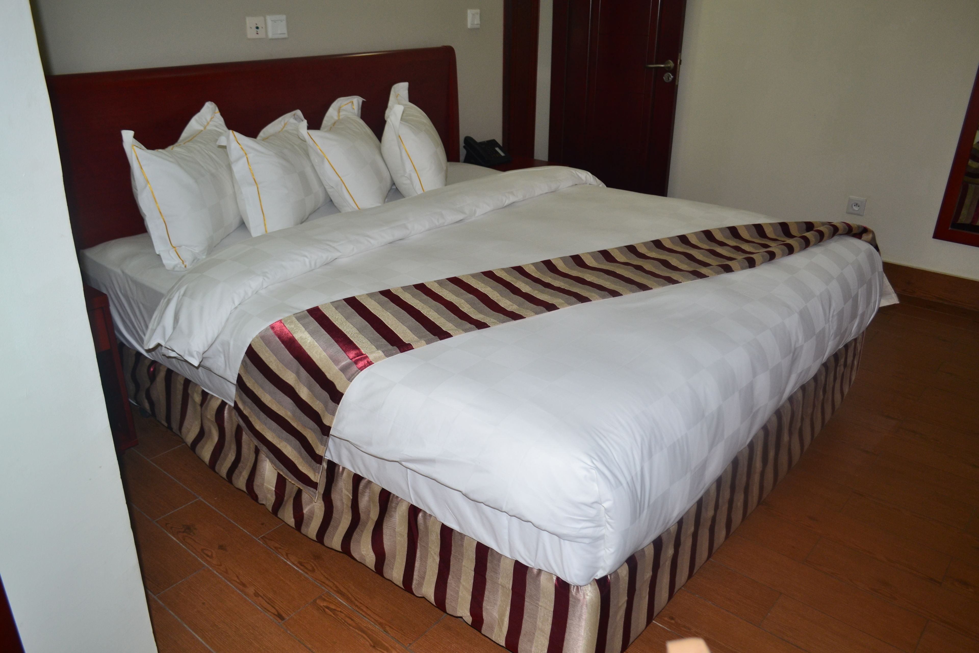 A neatly made bed with white linens and striped bedding, a wooden floor, and a red headboard.