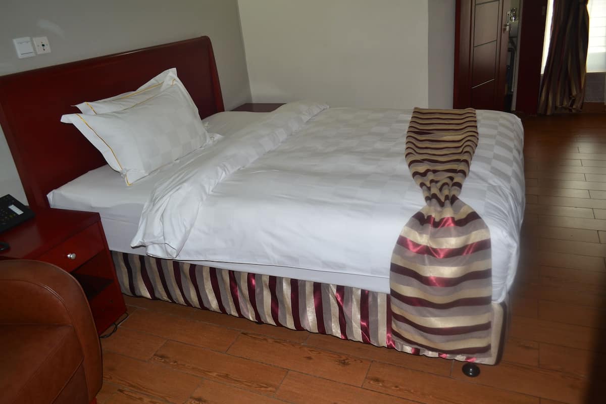 A neatly made bed with a striped bed skirt, a wooden headboard, and a white pillow.