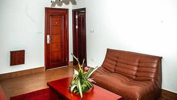 Un salon avec un canapé en cuir marron, une table basse rouge ornée d’une plante et un plancher en bois.