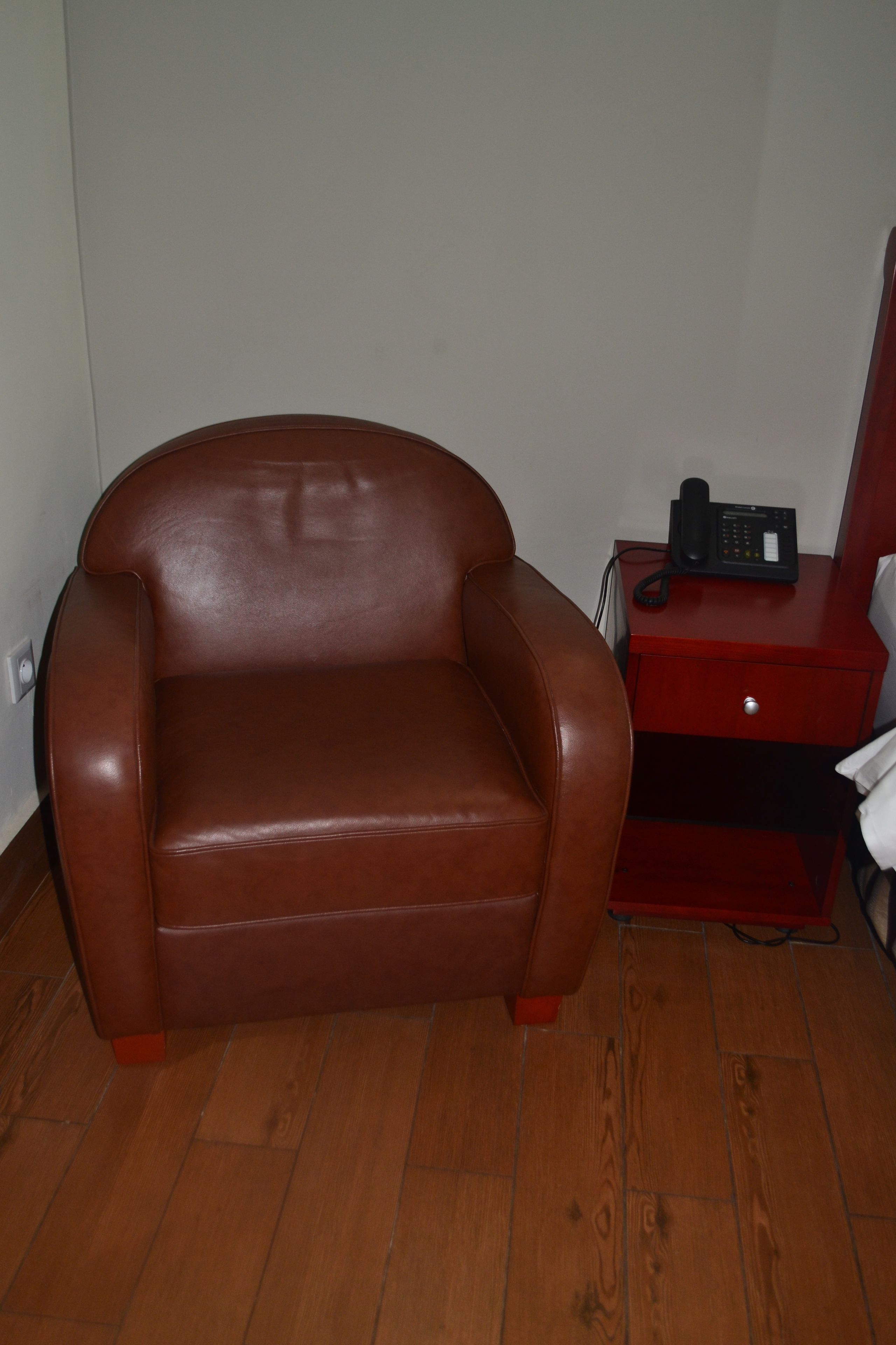 Un sillón de cuero marrón junto a un suelo de madera y una mesita de noche roja con un teléfono.