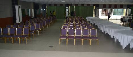 A conference room with rows of purple chairs and white tables, large windows, and a green curtain backdrop.