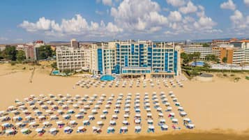 A hotel with multiple floors, a swimming pool, and a large beach area with numerous sunbeds.