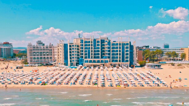 Un hôtel situé en bord de mer, avec plusieurs étages, une grande piscine et de nombreux parasols de plage.