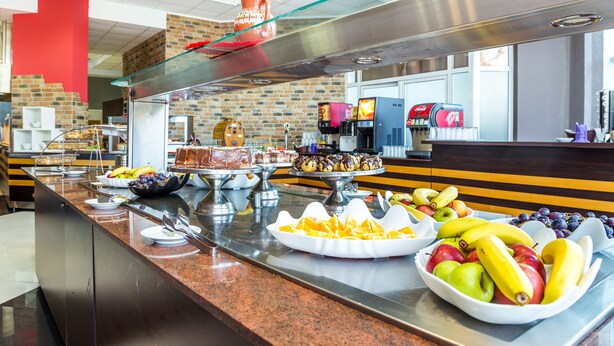 Un buffet proposant une variété de plats, notamment des fruits et des desserts, dans un cadre moderne avec des murs en briques et un comptoir en verre.