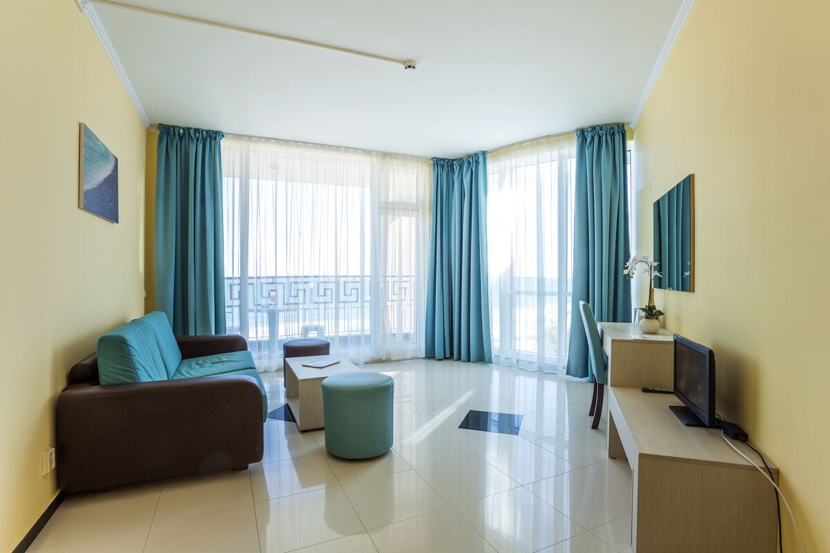Una habitación de hotel moderna con sofá, reposapiés, escritorio y televisión.
