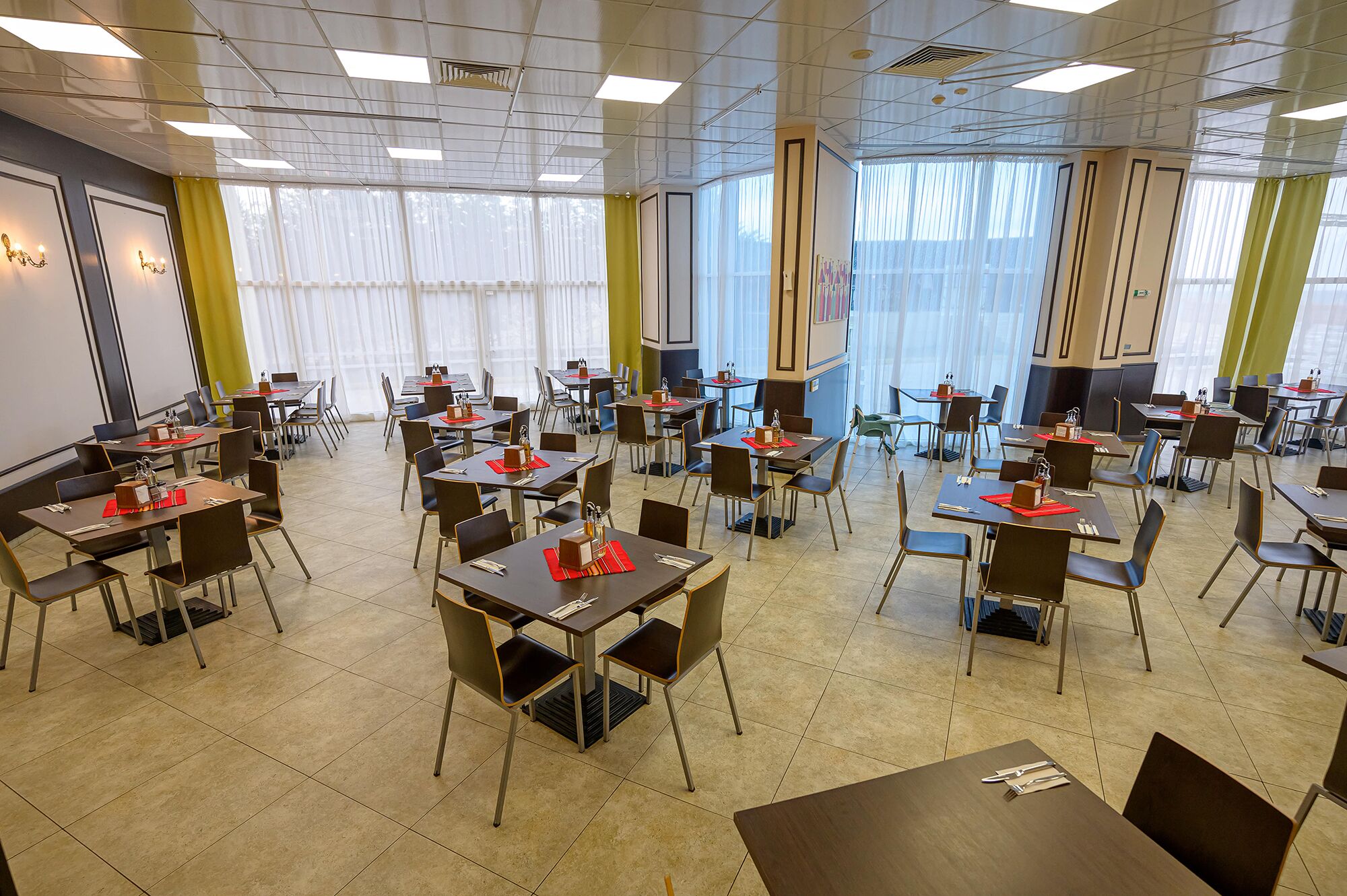Une salle de conférence équipée de plusieurs tables et chaises, de grandes fenêtres avec des rideaux et d’un tableau blanc fixé au mur.