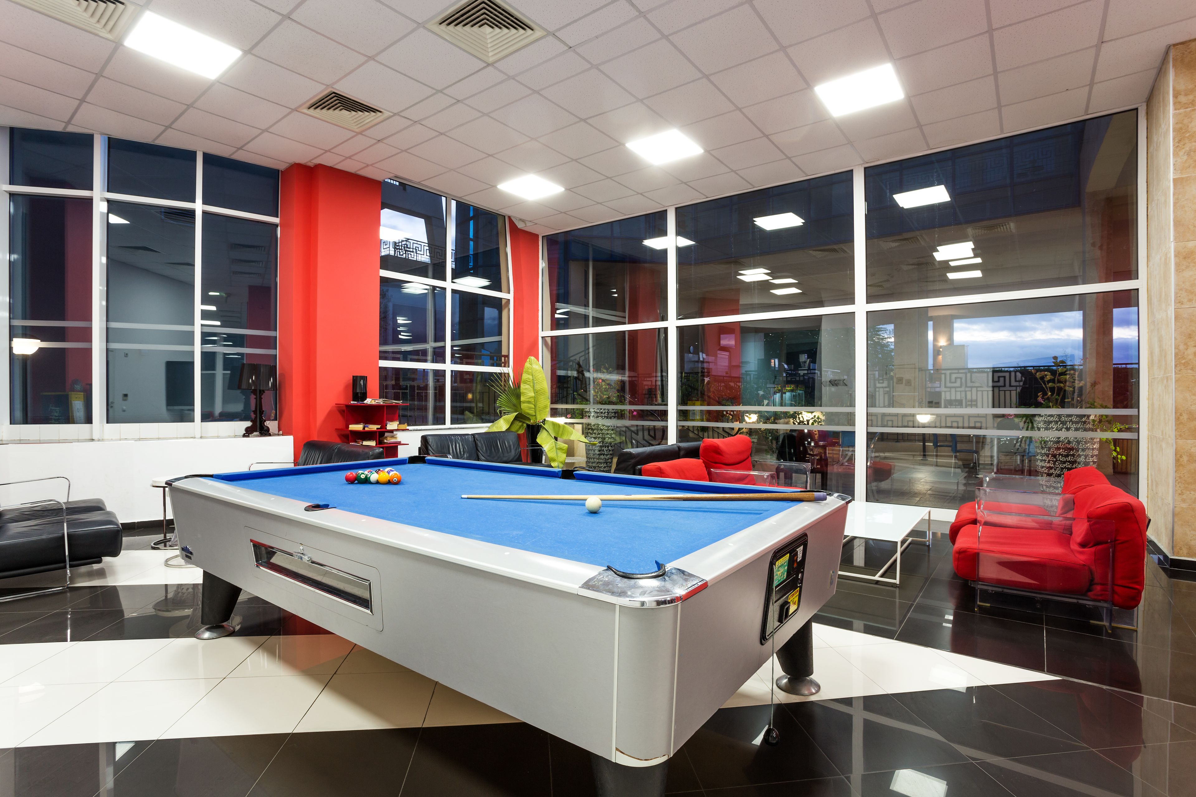 A pool table in a room with large windows, a red couch, and a view of the city.