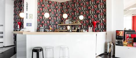 A lobby bar with a patterned wall, clear stools, and a counter with various bottles.