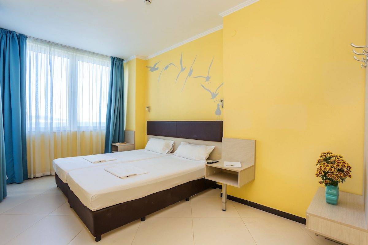 A hotel room with a large bed, a nightstand, a vase with flowers, and a wall mural.