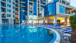 Une piscine avec des chaises longues, un restaurant et un immeuble à plusieurs étages doté de balcons.