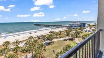 A beach view with a pier, a building with a sign, and a balcony railing.