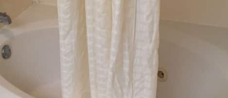 A bathtub with a white curtain, a small towel, and a soap dish.