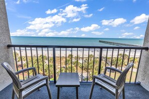 Ein Balkon mit zwei Stühlen und einem Tisch, mit Blick auf einen Strand und einen Steg.