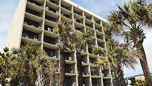 Un hotel de varios pisos con una fachada simétrica, balcones en cada planta y palmeras en primer plano.