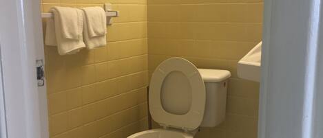 Une petite salle de bain propre, avec des toilettes, des murs recouverts de carreaux jaunes et un sol blanc.
