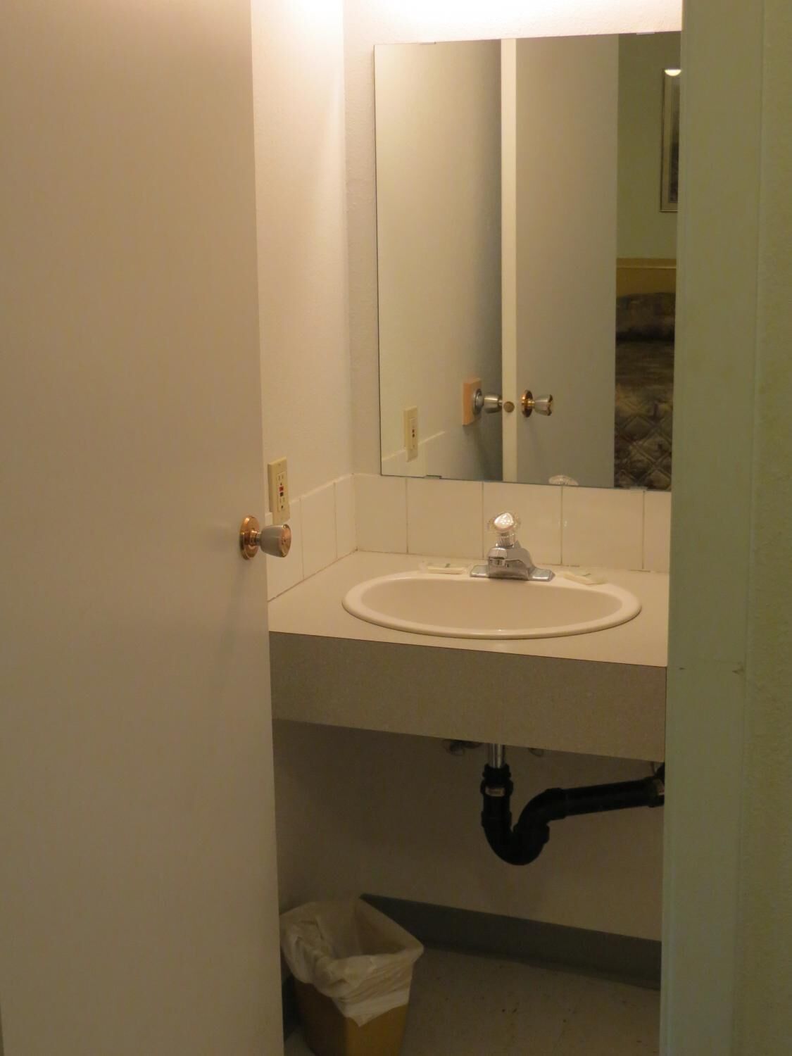 A bathroom with a white sink, a mirror, and a door with a brass handle.