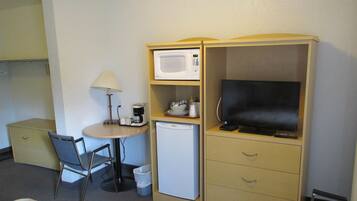 A compact hotel room with a bed, a desk with a lamp, a microwave, a small refrigerator, a television, and a chair.