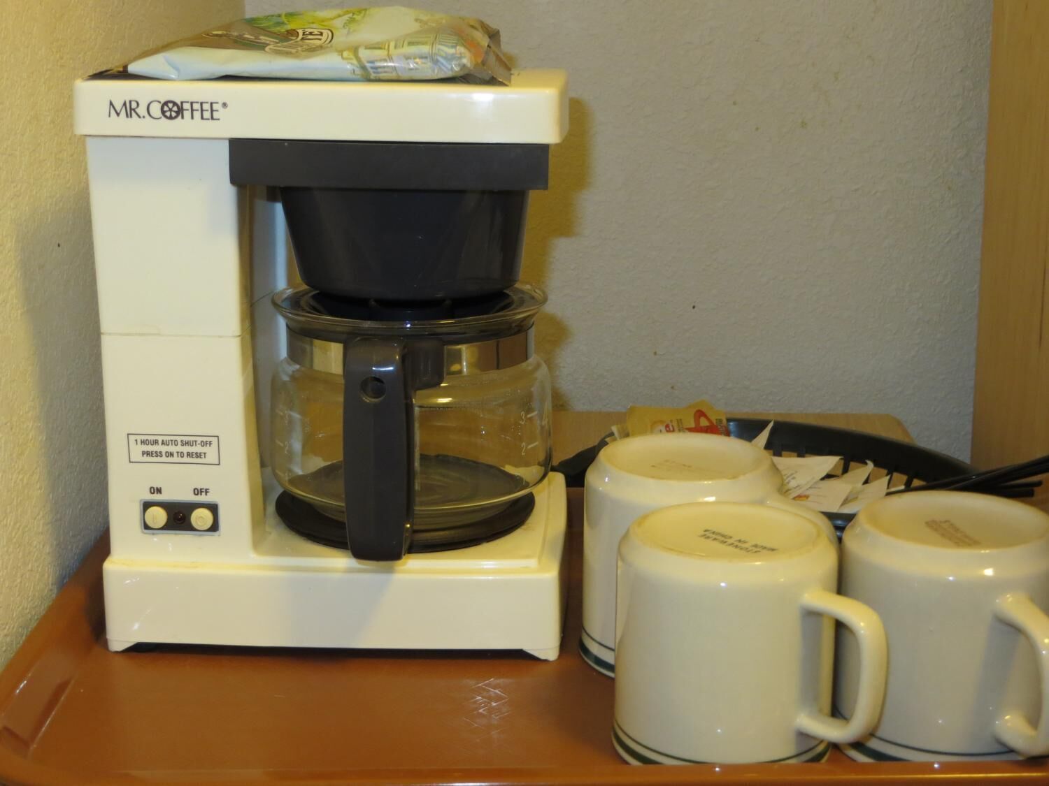 A Mr. Coffee coffee maker with a glass carafe and two white mugs on a wooden table.