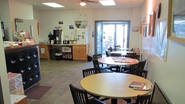 A dining area with round tables and chairs, a kitchen area with a refrigerator and microwave, and a door leading outside.