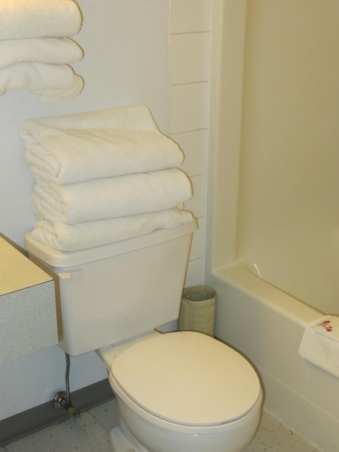 A bathroom with a toilet, a stack of white towels, a toilet paper holder, and a bathtub.