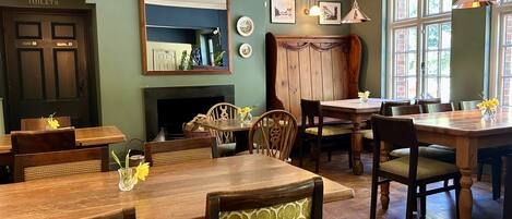 Un espace repas avec des tables et des chaises en bois, une cheminée et un miroir au mur.