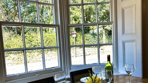 A dining table set for two with a view of a garden through large windows. - The Talbot (Blandford Forum)