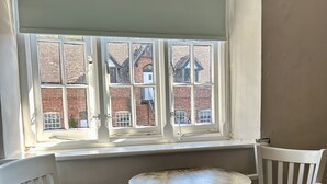 A corner room with a bay window overlooking a brick building. There is a round table with two chairs. - The Talbot (Blandford Forum)