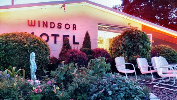 The exterior of the Windsor Hotel with a well-maintained garden, a seahorse sculpture, and outdoor seating. - Windsor Motel (Lake George)