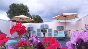 An outdoor patio area with two umbrellas, a table with chairs, and a variety of flowers. - Windsor Motel (Lake George)