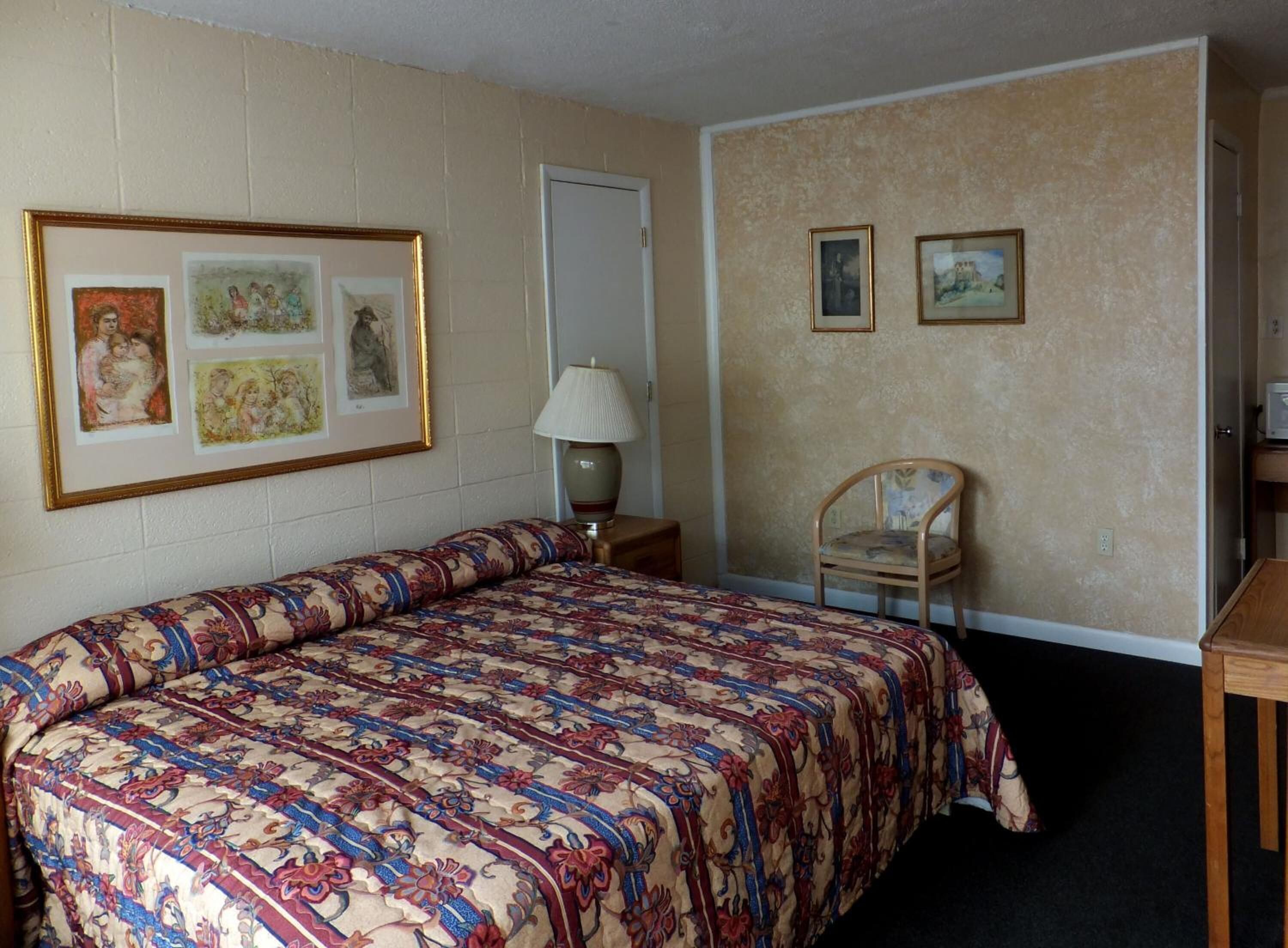 Una camera d'albergo con un letto grande, una poltrona, una lampada e due quadri appesi al muro.