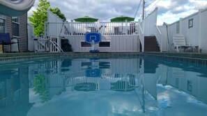 A swimming pool with a basketball hoop, white fence, and a covered area with chairs. - Windsor Motel (Lake George)