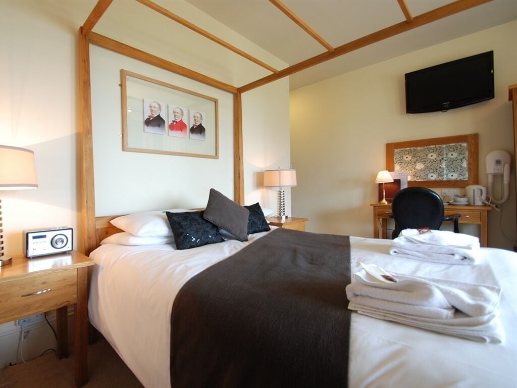 Une chambre d’hôtel comprenant un lit, des tables de chevet, un bureau, une chaise, un téléviseur et un tableau encadré au mur.