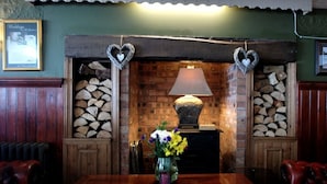 A cozy room with a wooden table, a vase with flowers, and a fireplace with heart-shaped decorations. - The Gladstone (Penmaenmawr)