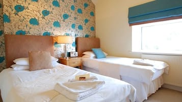 Quarto de hotel com duas camas, uma janela com cortinas azuis e um papel de parede com padrão floral.