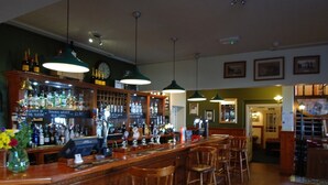 A bar area with wooden bar counters, multiple stools, hanging lights, and a variety of bottles and glasses. - The Gladstone (Penmaenmawr)