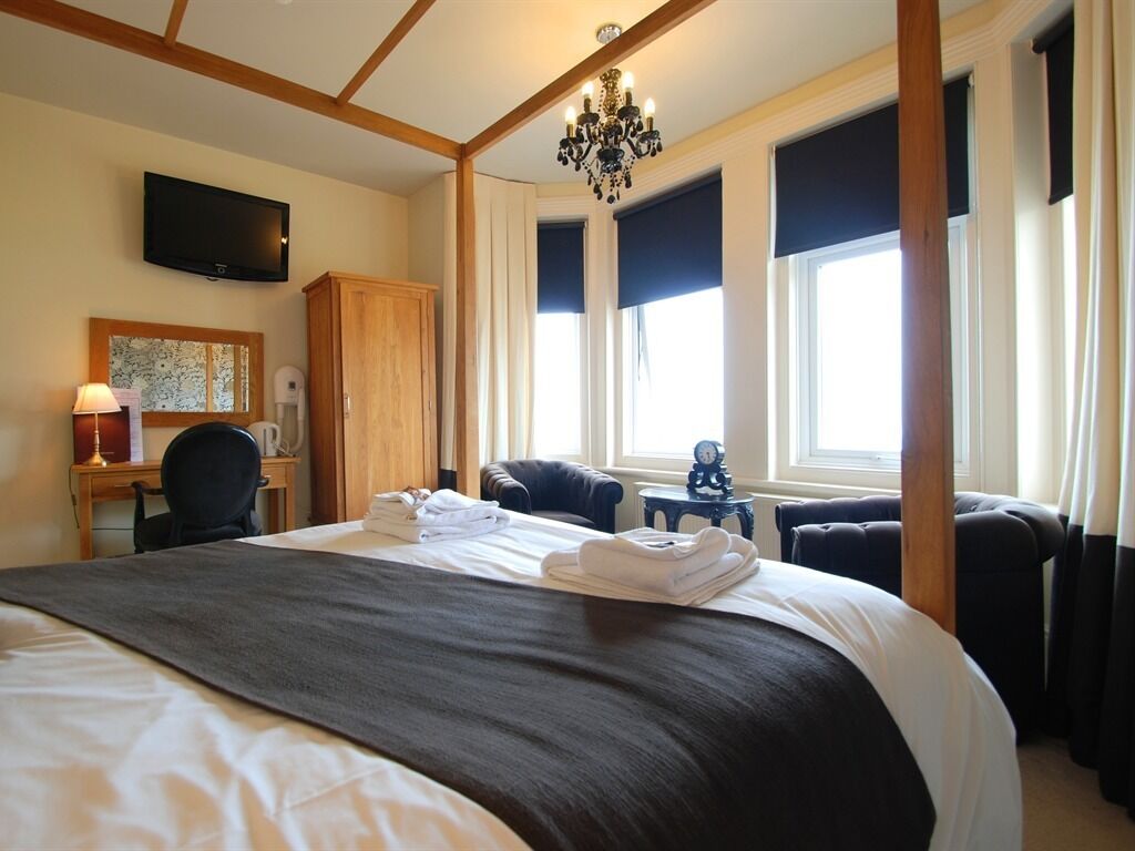 A hotel room with a large bed, a desk, a television, and a chandelier.