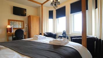 A hotel room with a large bed, a desk, a television, and a chandelier.