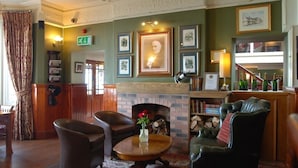 A cozy lobby with a fireplace, leather armchairs, a coffee table, and framed artwork on the walls. - The Gladstone (Penmaenmawr)