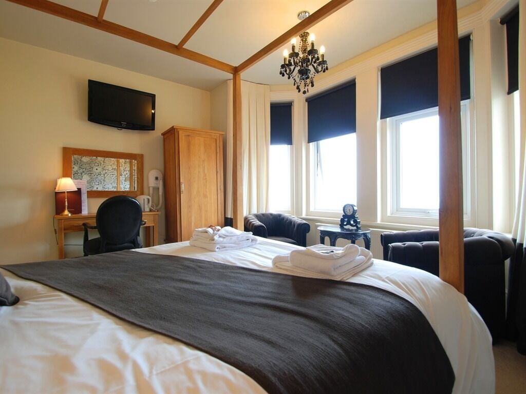 Habitación de hotel con una cama grande, un escritorio con lámpara, televisión en la pared y un candelabro.