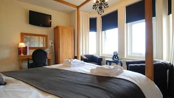 Habitación de hotel con una cama grande, un escritorio con lámpara, televisión en la pared y un candelabro.