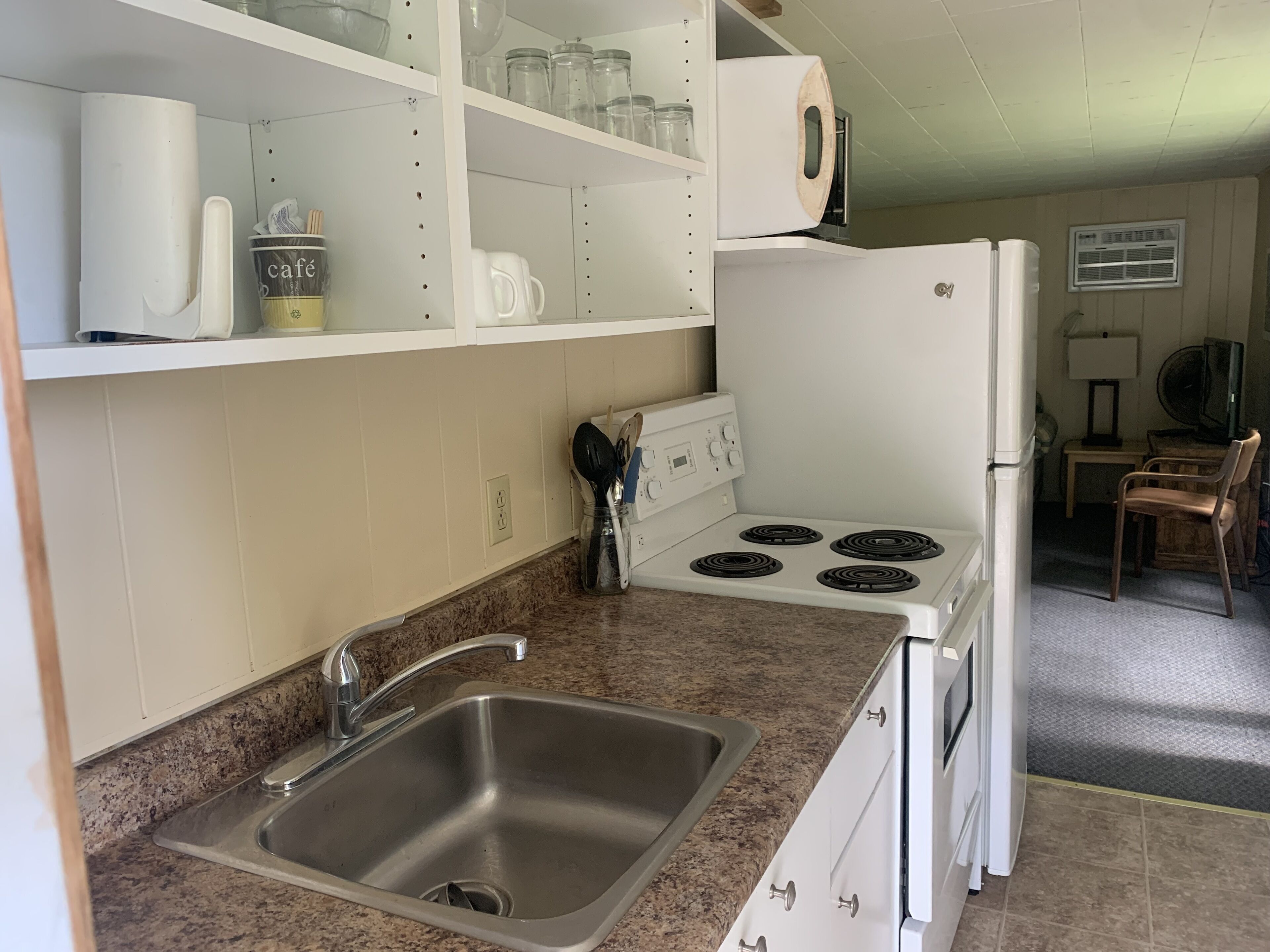 A kitchen with a stainless steel sink, a white stove, and a microwave on the countertop. There are shelves above the sink with various kitchen items.