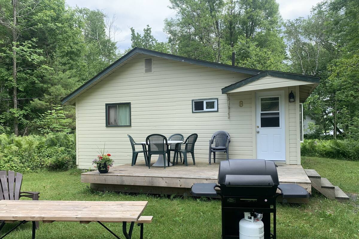 A small, single-story house with a porch, a table and chairs, and a grill.