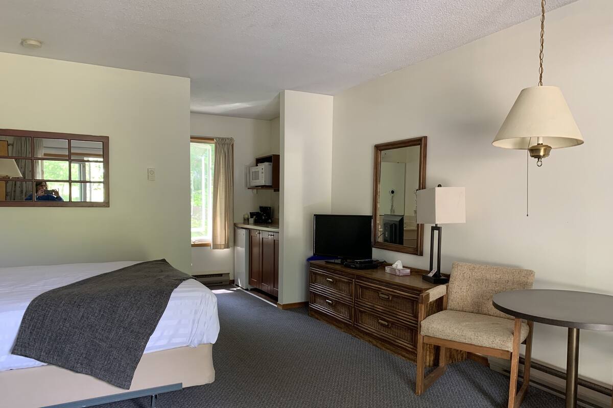 A hotel room with a bed, a desk with a television, a chair, a lamp, and a mirror.