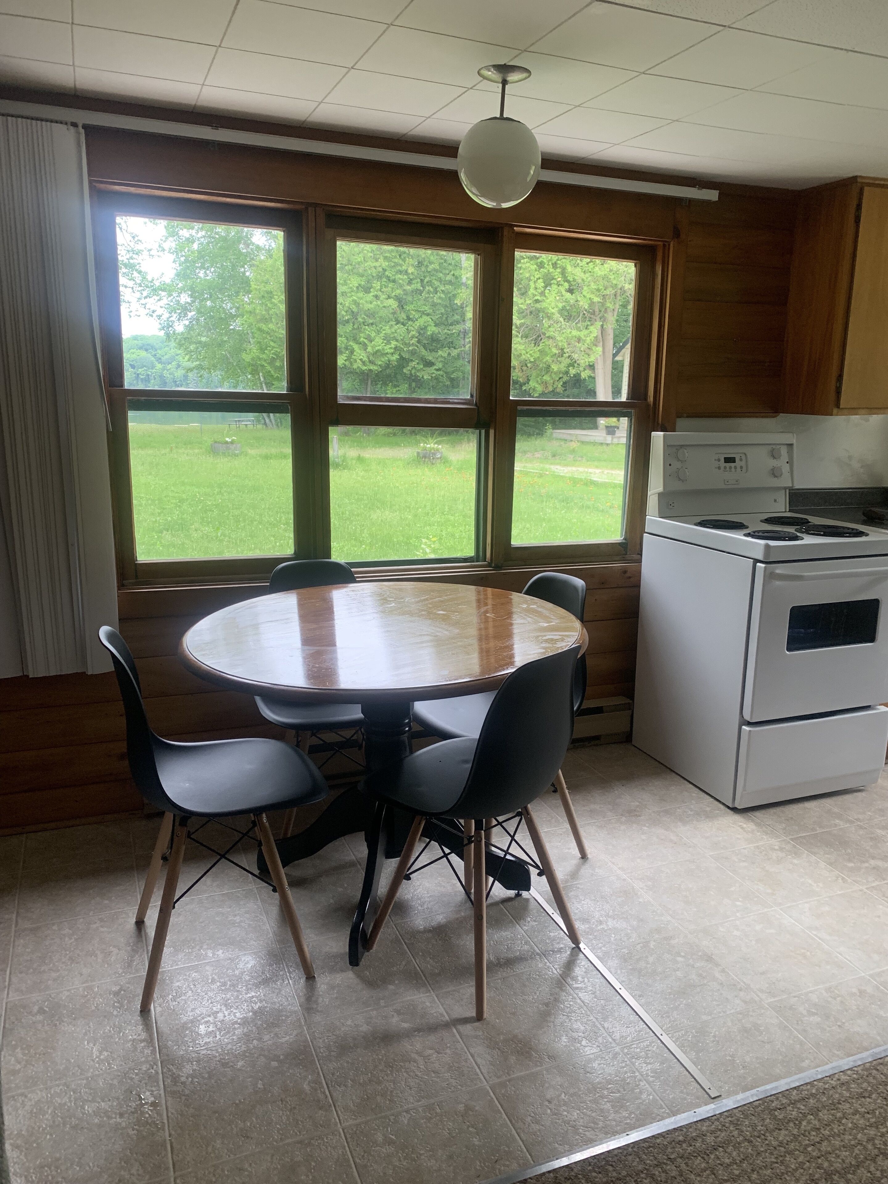 Une cuisine équipée d’une table et de chaises, d’une cuisinière et de grandes fenêtres donnant sur un espace verdoyant.